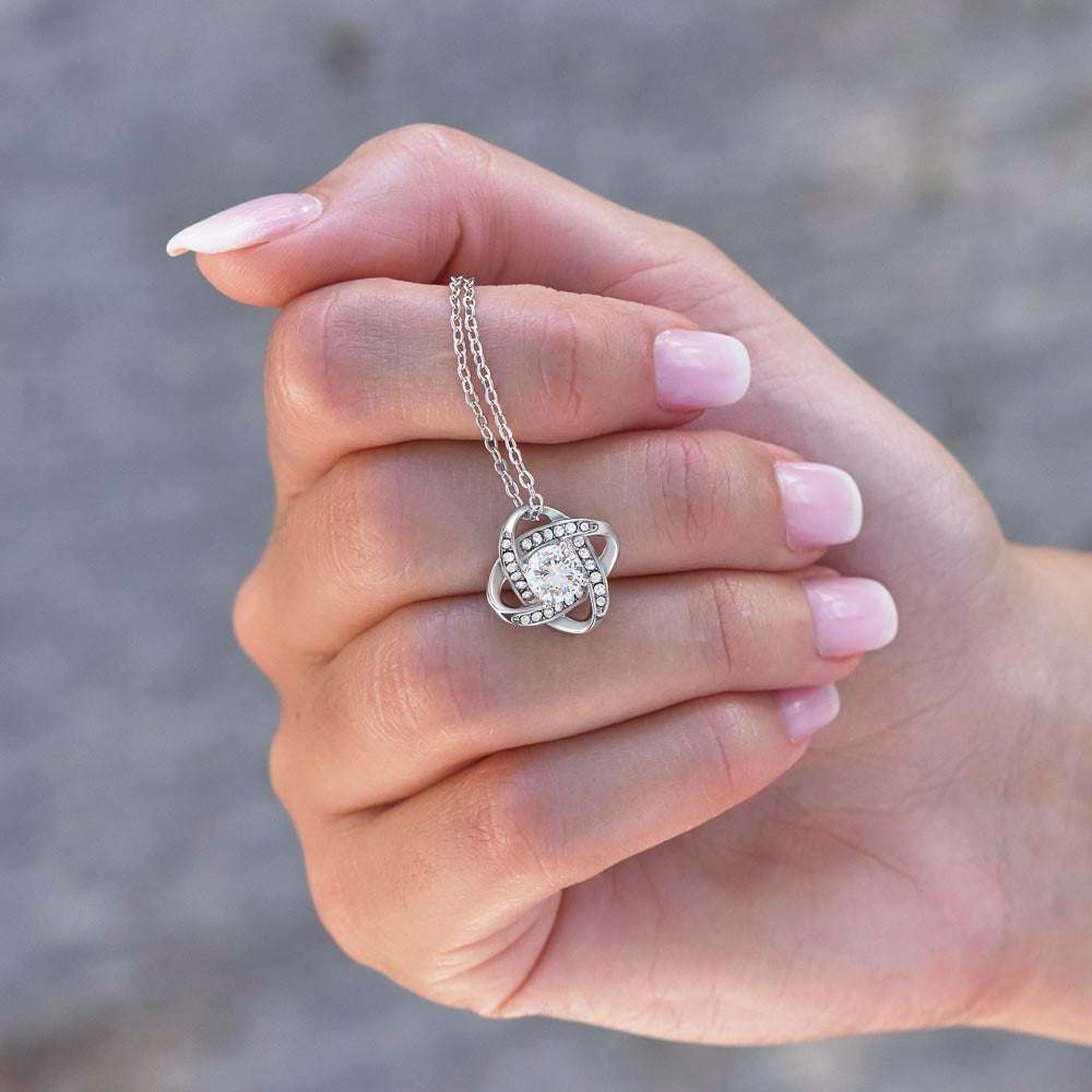 white gold love knot necklace in a model's hand