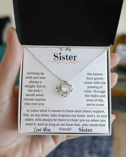 a white gold love knot necklace in a hand.