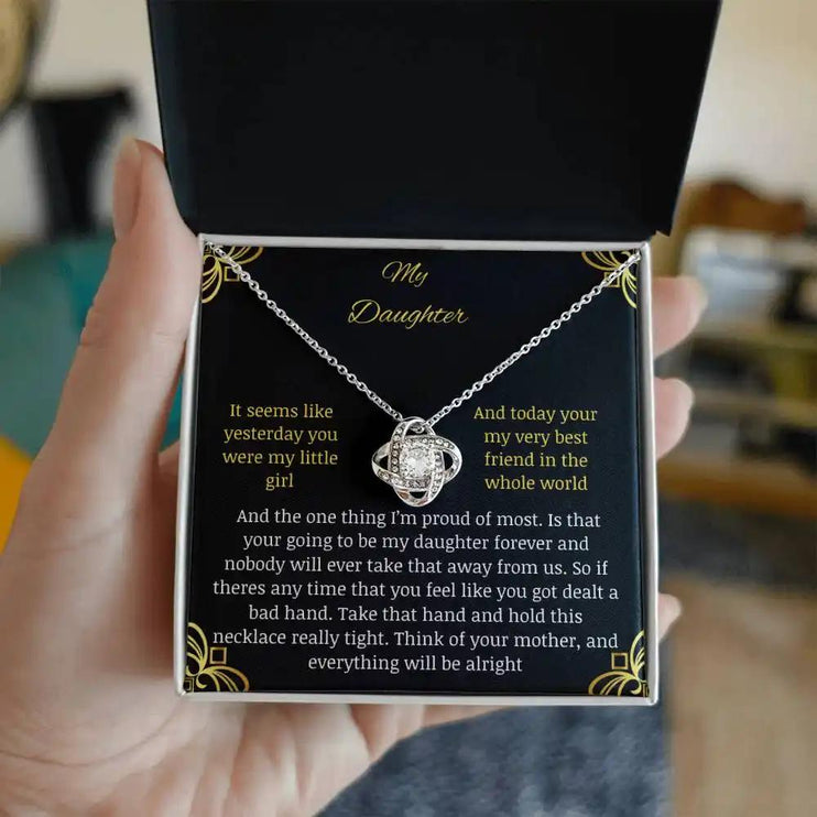 Love Knot Necklace with a white gold charm in a two-tone box with a to daughter from mom greeting card held in hand and away from