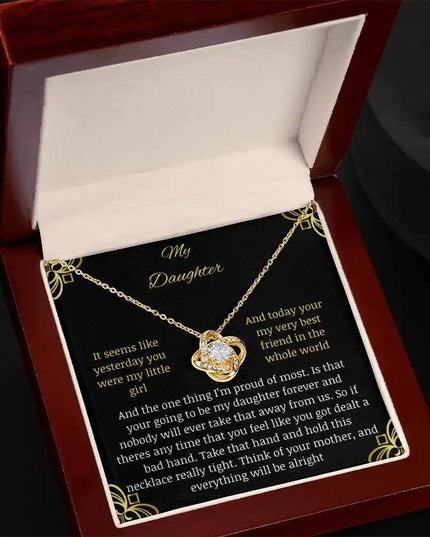 Love Knot Necklace with a yellow gold charm in a mahogany box tilted right with a to daughter from mom greeting card with black background
