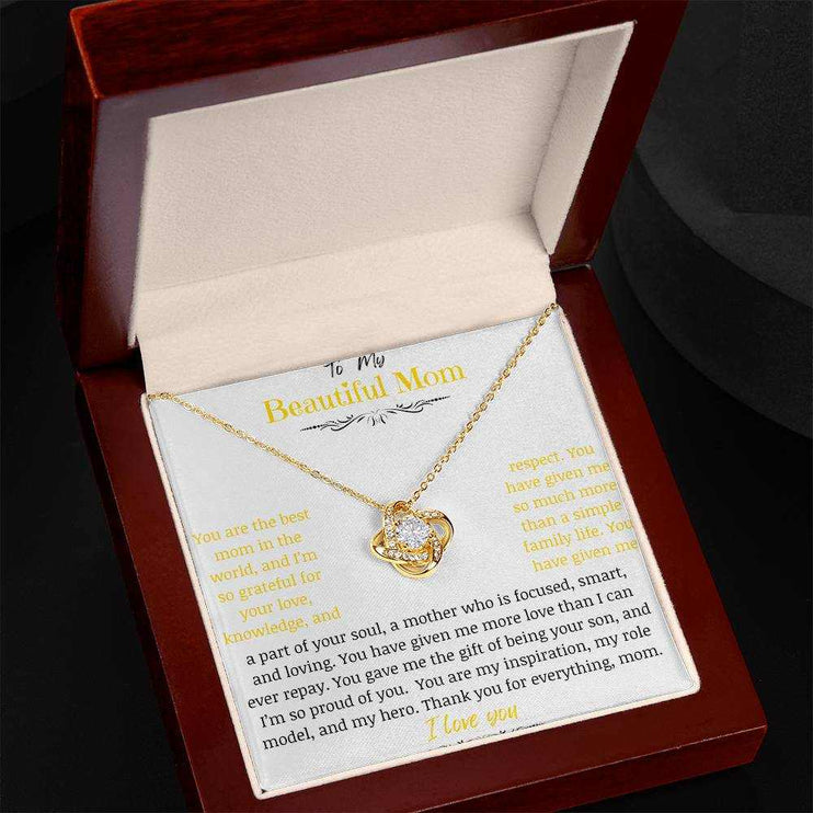 A yellow gold love knot necklace in a mahogany box angled to left