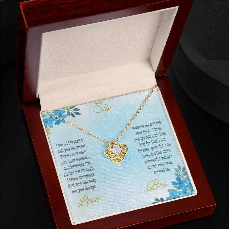 Love Knot Necklace with a yellow gold pendant on a To Sis from Bro greeting card inside of a mahogany box angled slightly to left side