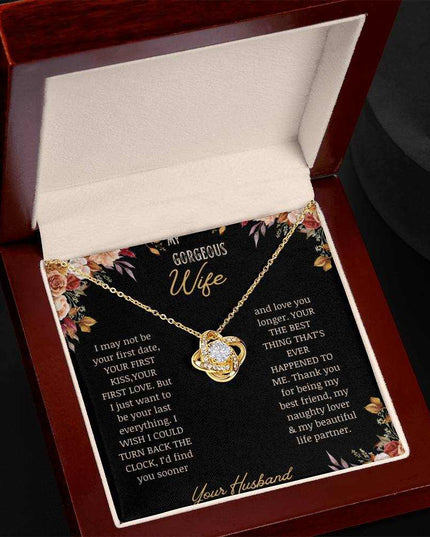 A yellow gold love knot necklace on a to wife greeting card in a mahogany box angled to the left