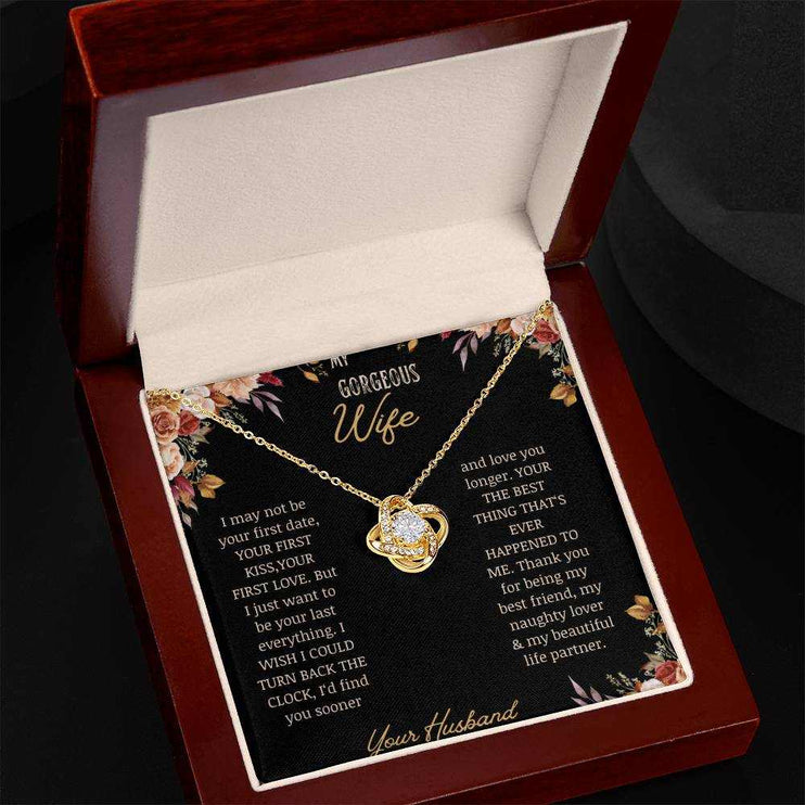 A yellow gold love knot necklace on a to wife greeting card in a mahogany box angled to the left
