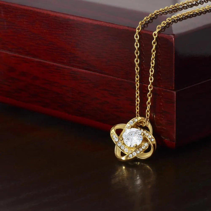 yellow gold love knot necklace on top of closed mahogany box