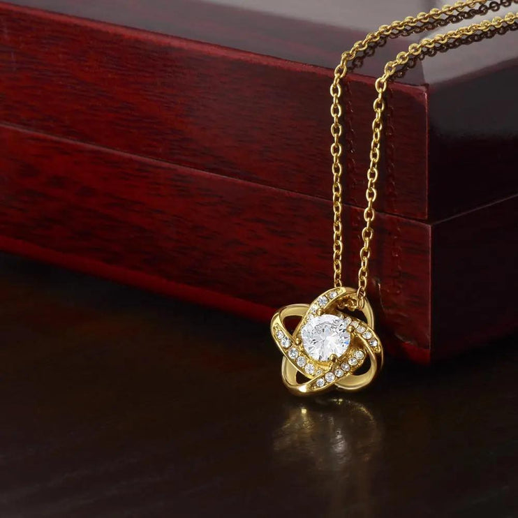yellow gold love knot necklace on top of a mahogany box 