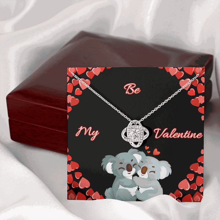 14k white gold love knot necklace on a card leaning on a mahogany box