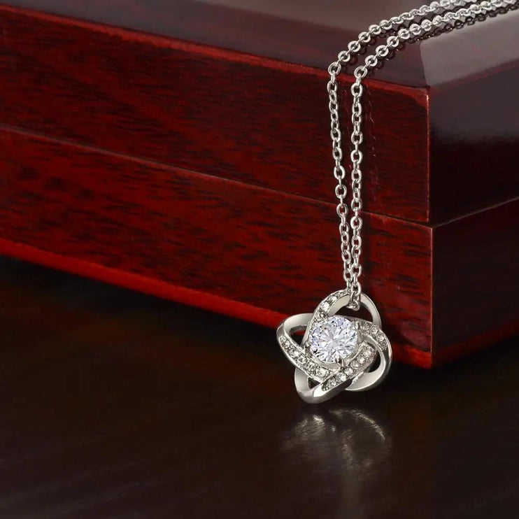 white gold love knot necklace on top of a mahogany box