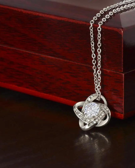 white gold love knot necklace on top of mahogany box