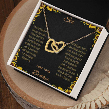 Interlocking Hearts Necklace with a gold variant on a To Sis from Brother greeting card inside a two-tone box sitting on a stump