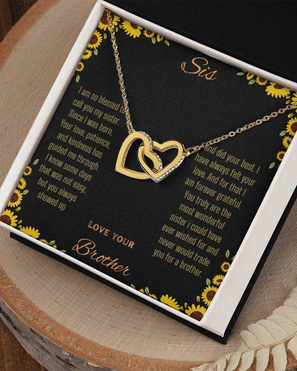 Interlocking Hearts Necklace with a gold variant on a To Sis from Brother greeting card inside a two-tone box sitting on a stump
