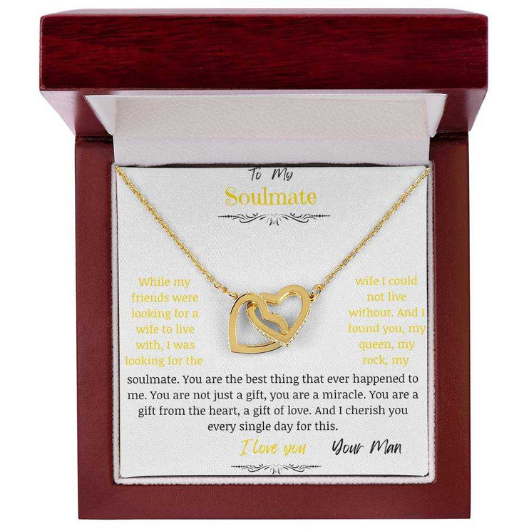 A gold interlocking hearts necklace up close in a mahogany box