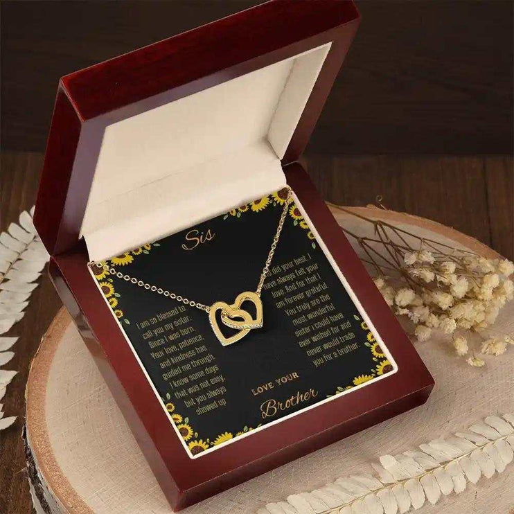 Interlocking Hearts Necklace with a gold variant on a To Sis from Brother greeting card inside a mahogany box sitting on a stump angled to right side