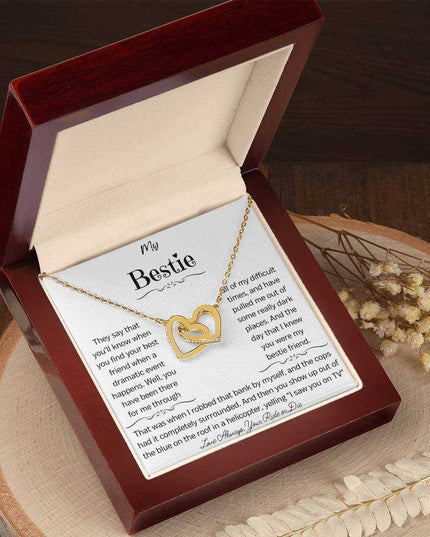 a gold interlocking hearts necklace in a mahogany box on a stump