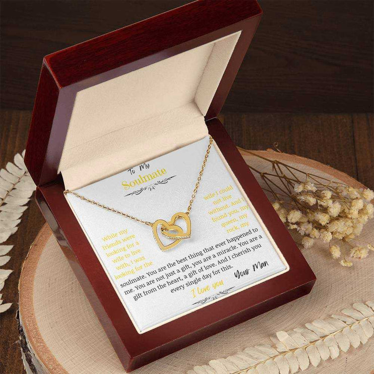 A gold interlocking hearts necklace up close on a stump in a mahogany box