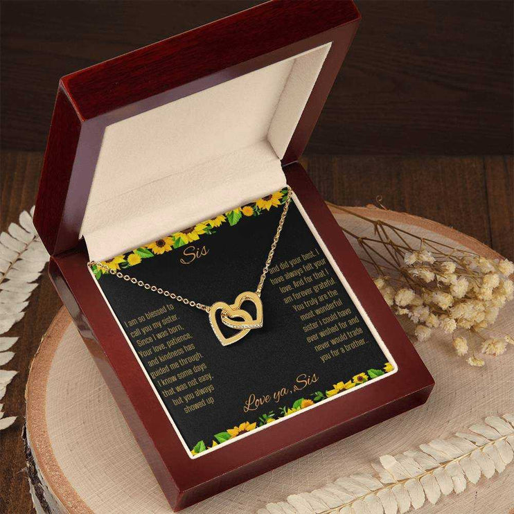Interlocking Hearts Necklace with a gold on gold variant on a To Sis from Sis greeting card close up in a mahogany box angled to the left side on a stump