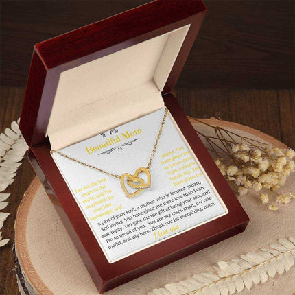 A gold gold interlocking hearts necklace up close in a mahogany box on a stump