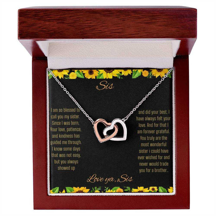 Interlocking Hearts Necklace with a rose gold variant on a To Sis from Sis greeting card close up in a mahogany box