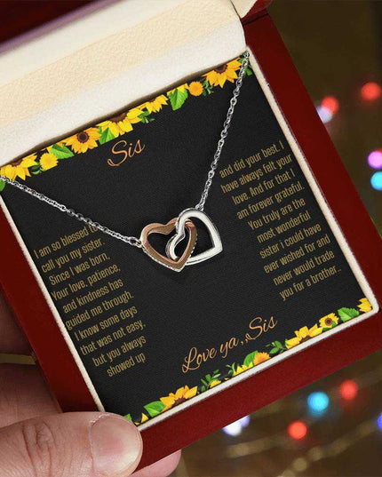 Interlocking Hearts Necklace with a rose gold variant on a To Sis from Sis greeting card close up in a mahogany box angled to the left side