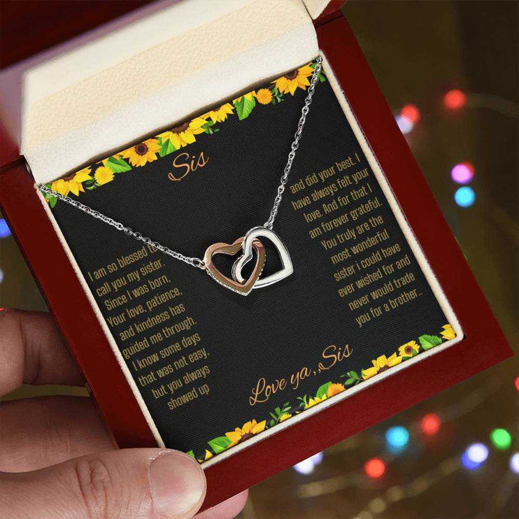 Interlocking Hearts Necklace with a rose gold variant on a To Sis from Sis greeting card close up in a mahogany box angled to the left side