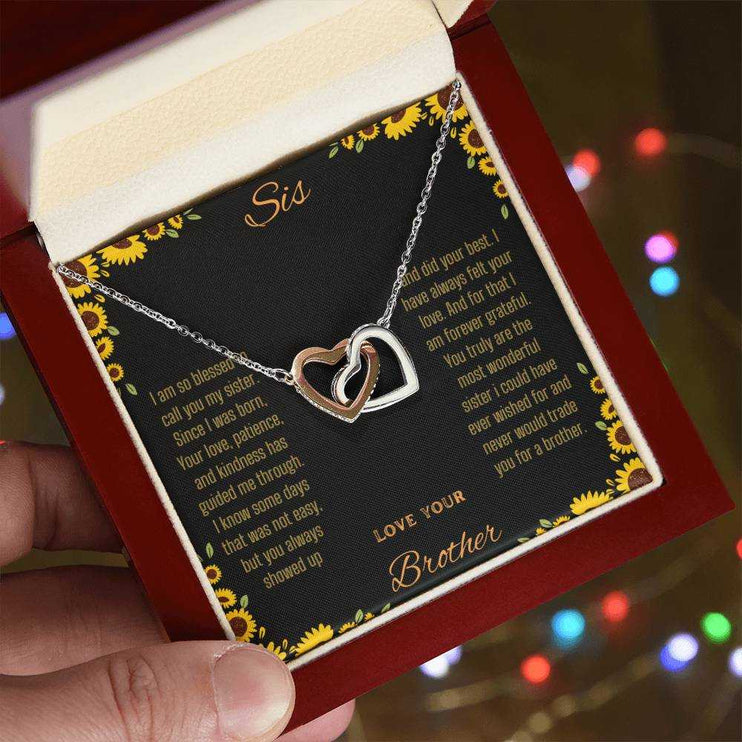 Interlocking Hearts Necklace with rose gold variant on a To Sis from Brother greeting card up close in models hand angled to right side
