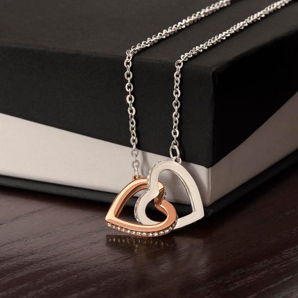 Interlocking Hearts Necklace with rose gold variant on a closed two-tone box on a black table