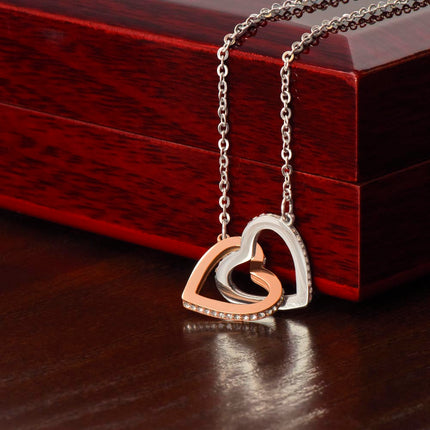 Interlocking Hearts Necklace with rose gold variant on a closed mahogany box on a black table