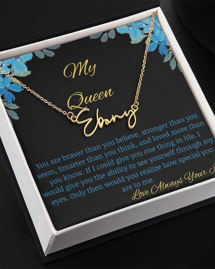 A yellow gold signature name necklace in a two-tone box with a to my queen greeting card angled to the left