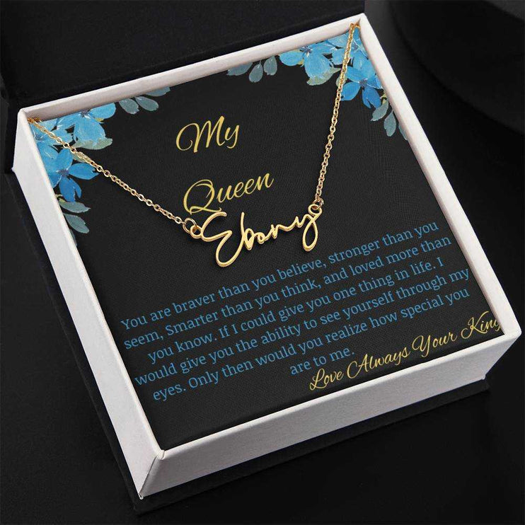 A yellow gold signature name necklace in a two-tone box with a to my queen greeting card angled to the left