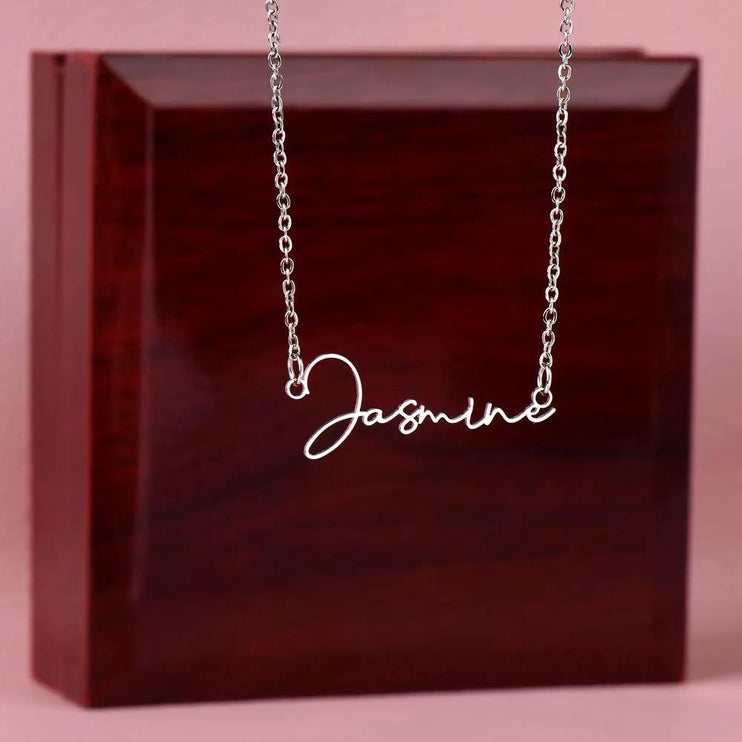 polished steel signature style name necklace on top of mahogany box