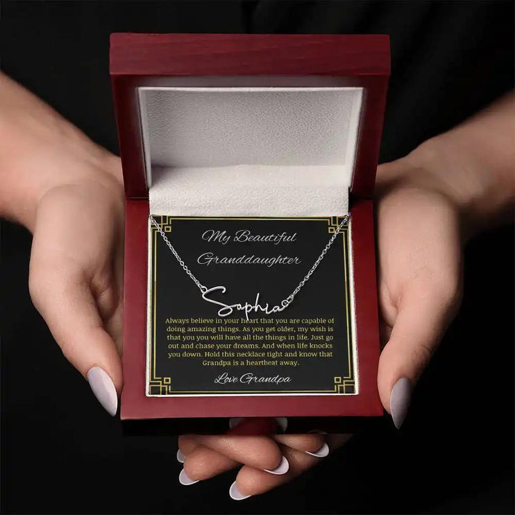 Signature Name Necklace with a polished stainless-steel finish on a to granddaughter from grandpa greeting card in a mahogany box in a models hands