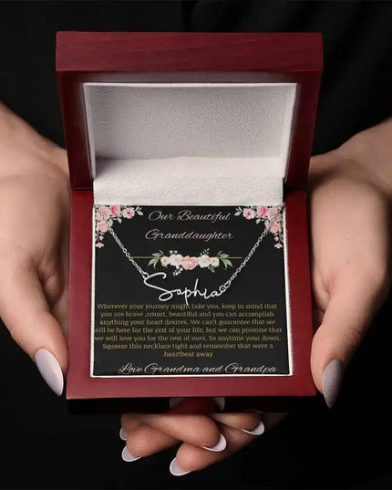 Signature Name Necklace with a yellow gold finish and a to granddaughter from grandma and grandpa greeting card in a mahogany box in a models hands