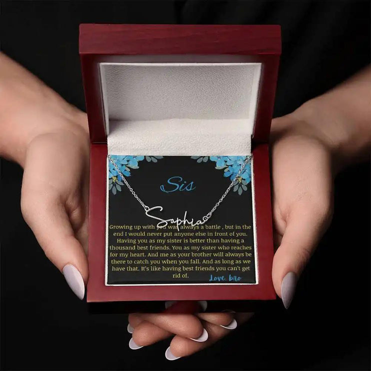 Signature Name Necklace with a polished stainless-steel charm on a to sis from bro greeting card in a mahogany box in a models hand