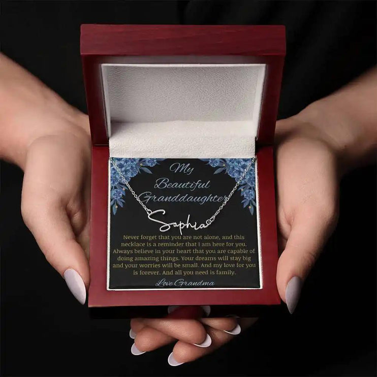Signature Name Necklace with a polished stainless-steel finish on a to my beautiful granddaughter from grandma greeting card in a mahogany box held in models hands
