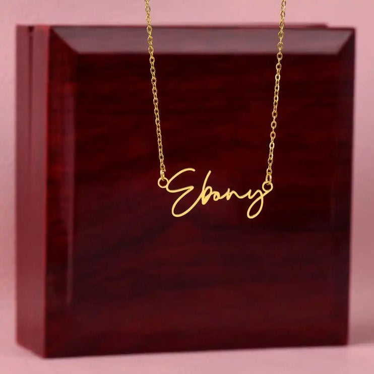 A yellow gold signature name necklace hanging on a mahogany box 