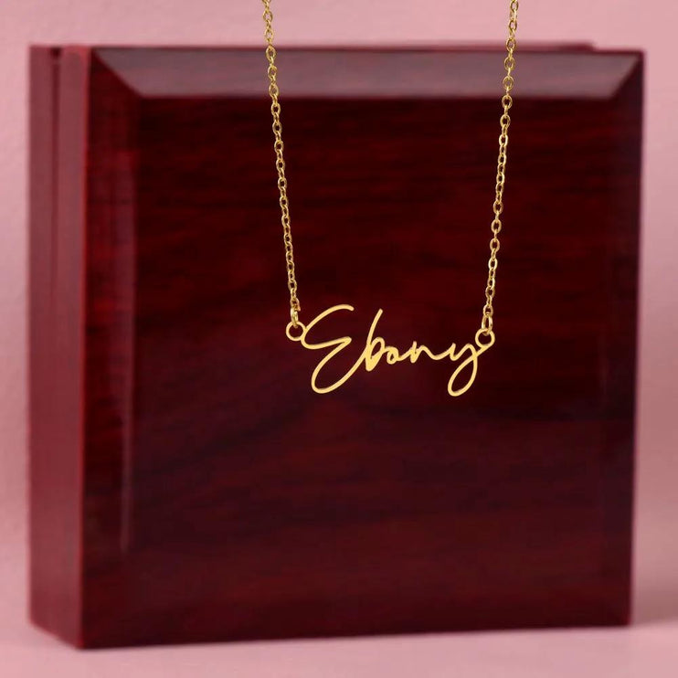 a yellow gold signature name necklace on top of a mahogany box.