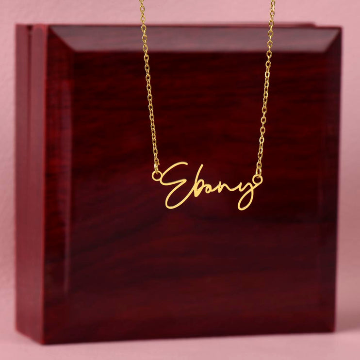 A yellow gold finish signature name necklace on top of a mahogany box.