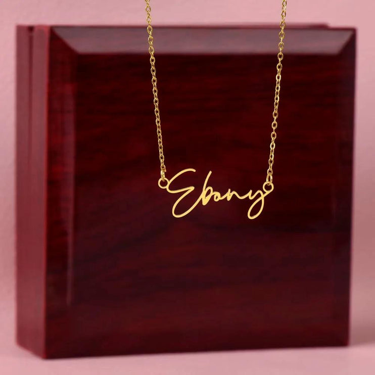 Signature Name Necklace with a yellow gold finish on top of a closed mahogany box