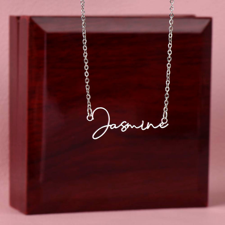 a polished stainless-steel signature name necklace on top of a two-tone box