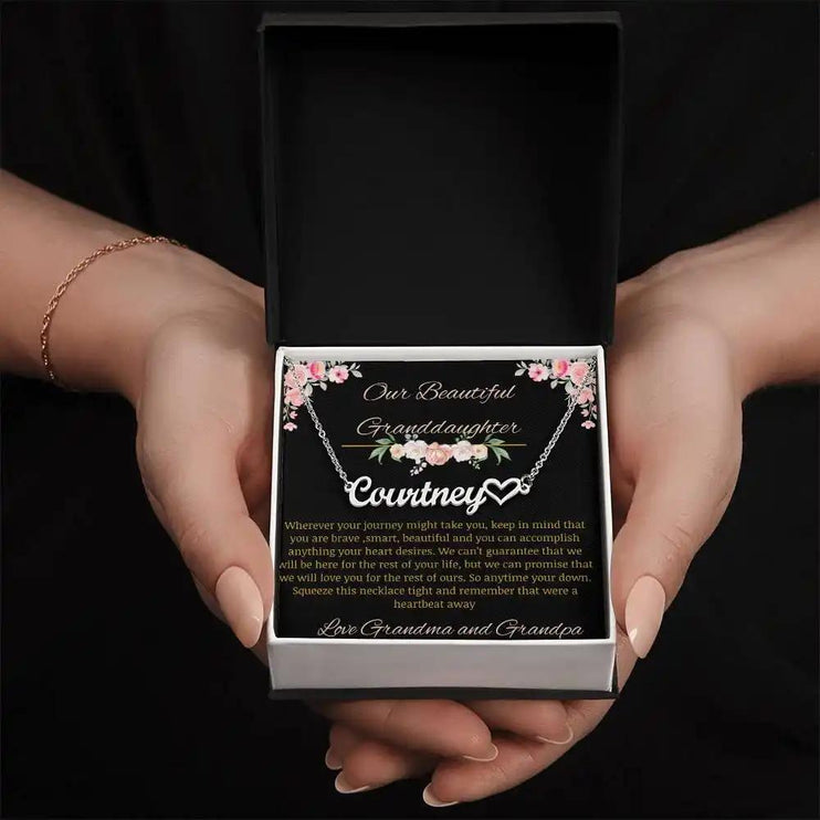 Name Heart Necklace with a polished stainless-steel finish on a to granddaughter from grandma and grandpa greeting card in a two-tone box in a models hands