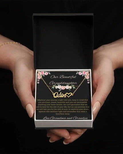 Name Heart Necklace with a yellow gold finish on a to granddaughter from grandma and grandpa greeting card in a two-tone box in a models hands