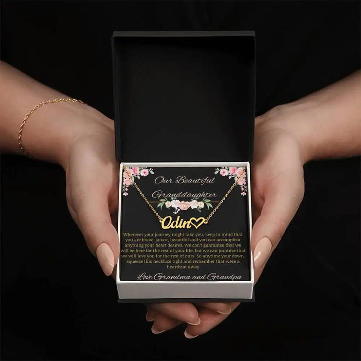 Name Heart Necklace with a yellow gold finish on a to granddaughter from grandma and grandpa greeting card in a two-tone box in a models hands