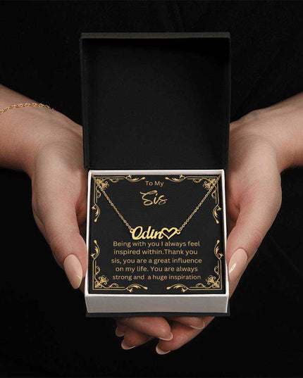 Name Heart Necklace with a yellow gold finish variant on a To Sis greeting card inside a two-tone box up close view in the hands of a model