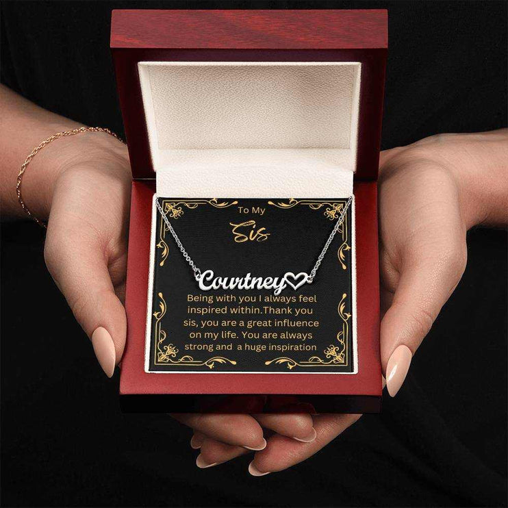 Name Heart Necklace with a polished stainless-steel variant on a To Sis greeting card inside a mahogany box up close view in the hands of a model