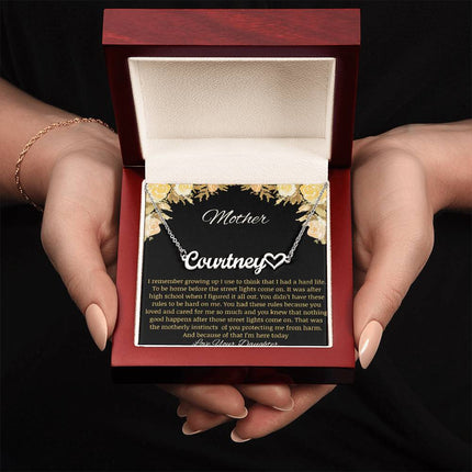 A polished stainless-steel name heart necklace in a mahogany box being held.