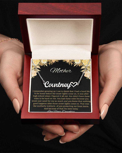 A polished stainless-steel name heart necklace in a mahogany box being held.