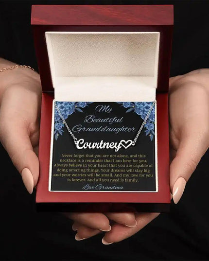 Name Heart Necklace with a polished stainless-steel charm on a to granddaughter from grandma greeting card in a mahogany in a models hands
