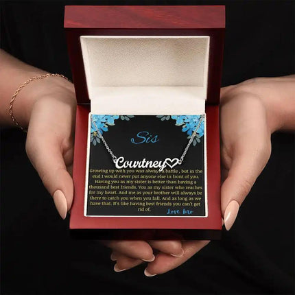 Name Heart Necklace with a polished stainless-steel charm with a to sis from bro greeting card in a mahogany box in a models hand