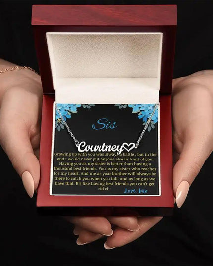 Name Heart Necklace with a polished stainless-steel charm with a to sis from bro greeting card in a mahogany box in a models hand