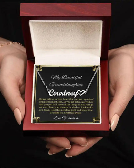 Name Heart Necklace with a polished stainless-steel charm on a to granddaughter from grandpa greeting card in a mahogany box in a models hands